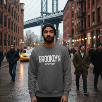 Man wearing a gray sweatshirt with 'Brooklyn New York' text, standing in an urban street scene with the Manhattan Bridge in the background.